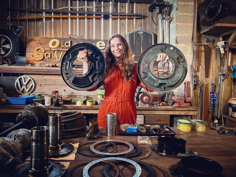 Woman in orange overalls in a workshop holding up car parts