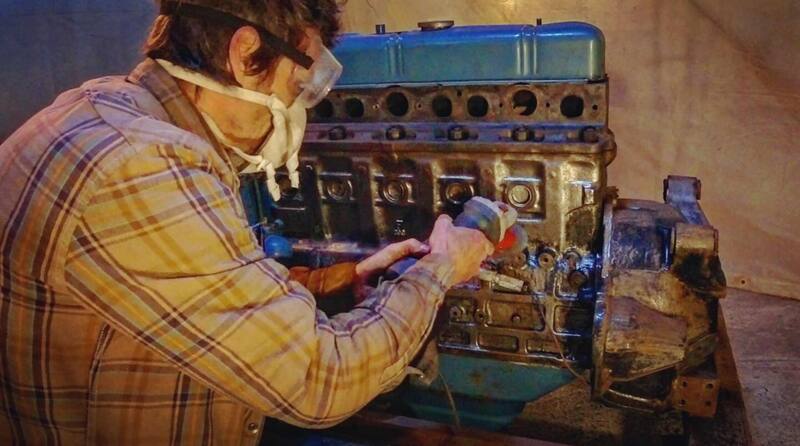 Man grinding the paint off of a truck petrol engine