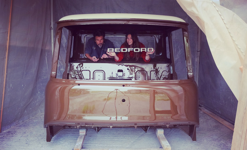 Man and woman in a restored Bedford truck cab painted in cream and brown