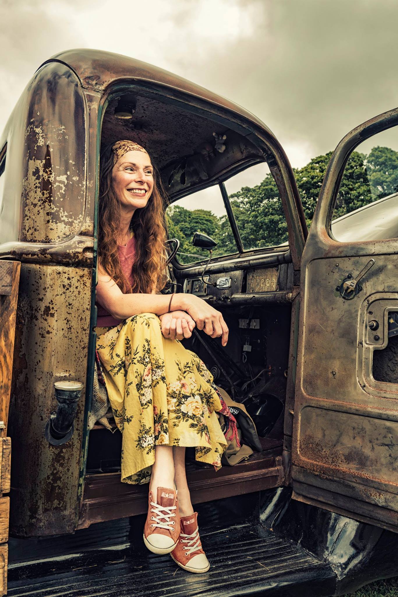 Woman in a yellow dress sitting in the doorway of a rusty vintage Ford truck
