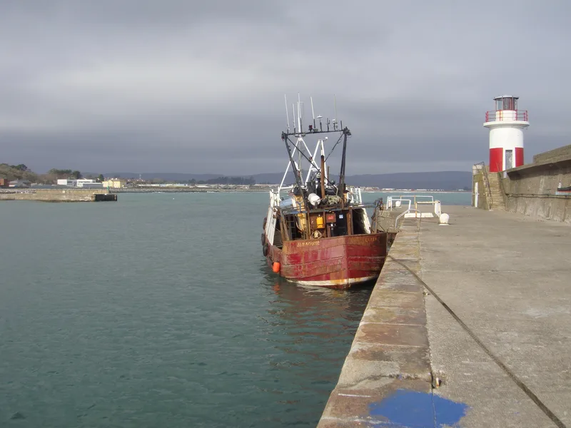 Old red fishing trawler moored against harbour wall at Wicklow in Southern Ireland