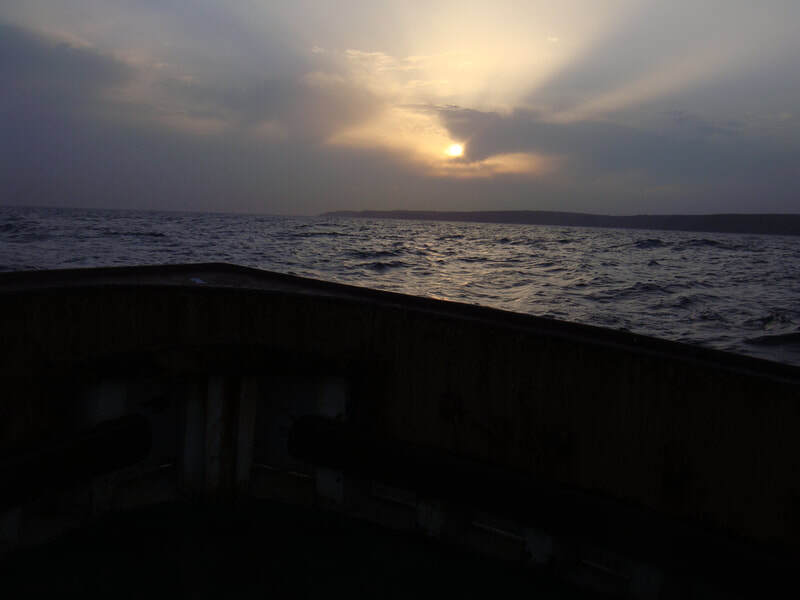 View of a sunset at sea from the deck of a wooden boat