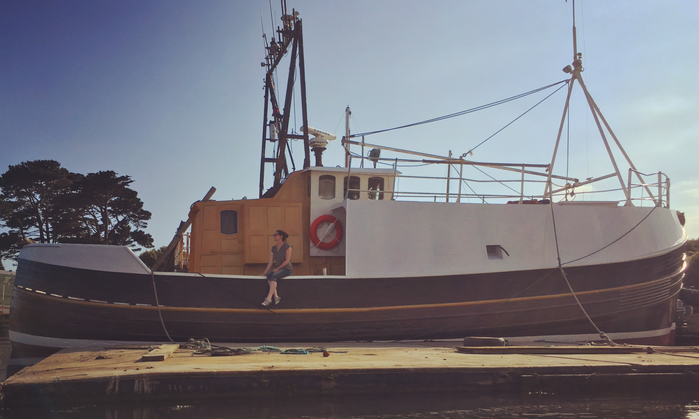 Restored fishing trawler moored up with a woman sitting on the side of the boat on a sunny day