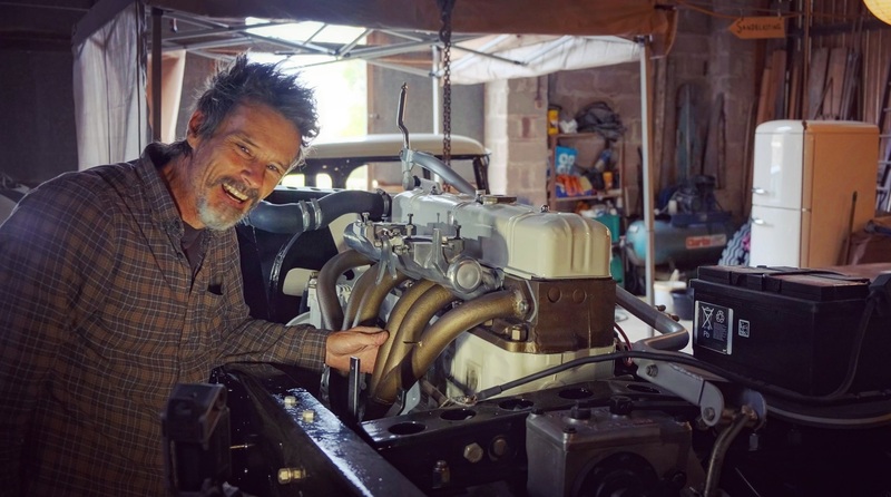 Man standing smiling next to the petrol engine in a 1970s Bedford truck
